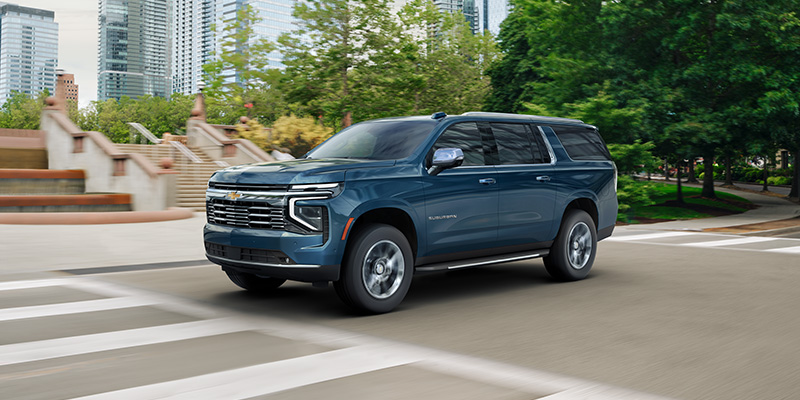 Blue Chevrolet Suburban driving on a city street.