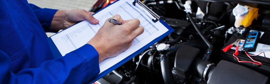 Mechanic inspecting a car engine and noting details on a checklist
